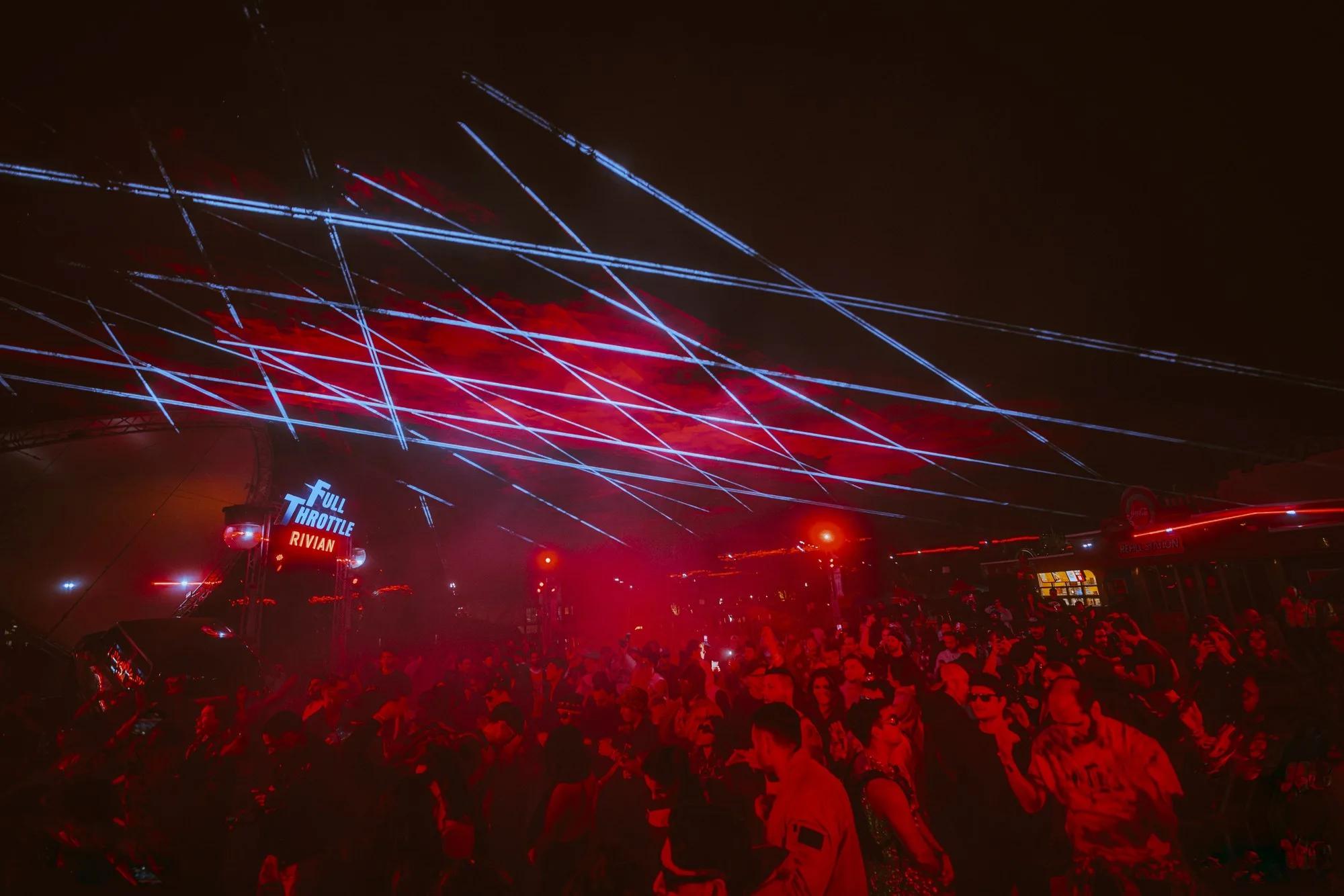 Fan of red and white lasers sweeping over a packed festival crowd at night