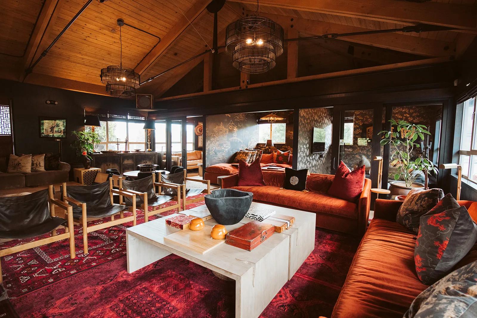Lodge lounge with vaulted wood ceiling, wire-cage pendants, rust velvet sofas, red rugs and white coffee table